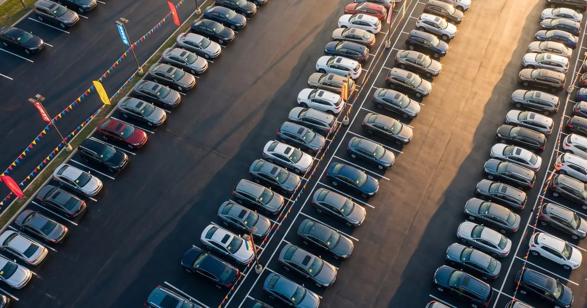 Aerial view of a new-car dealership lot with vehicles in neat rows and sale flags, representing the best time of year to buy a car